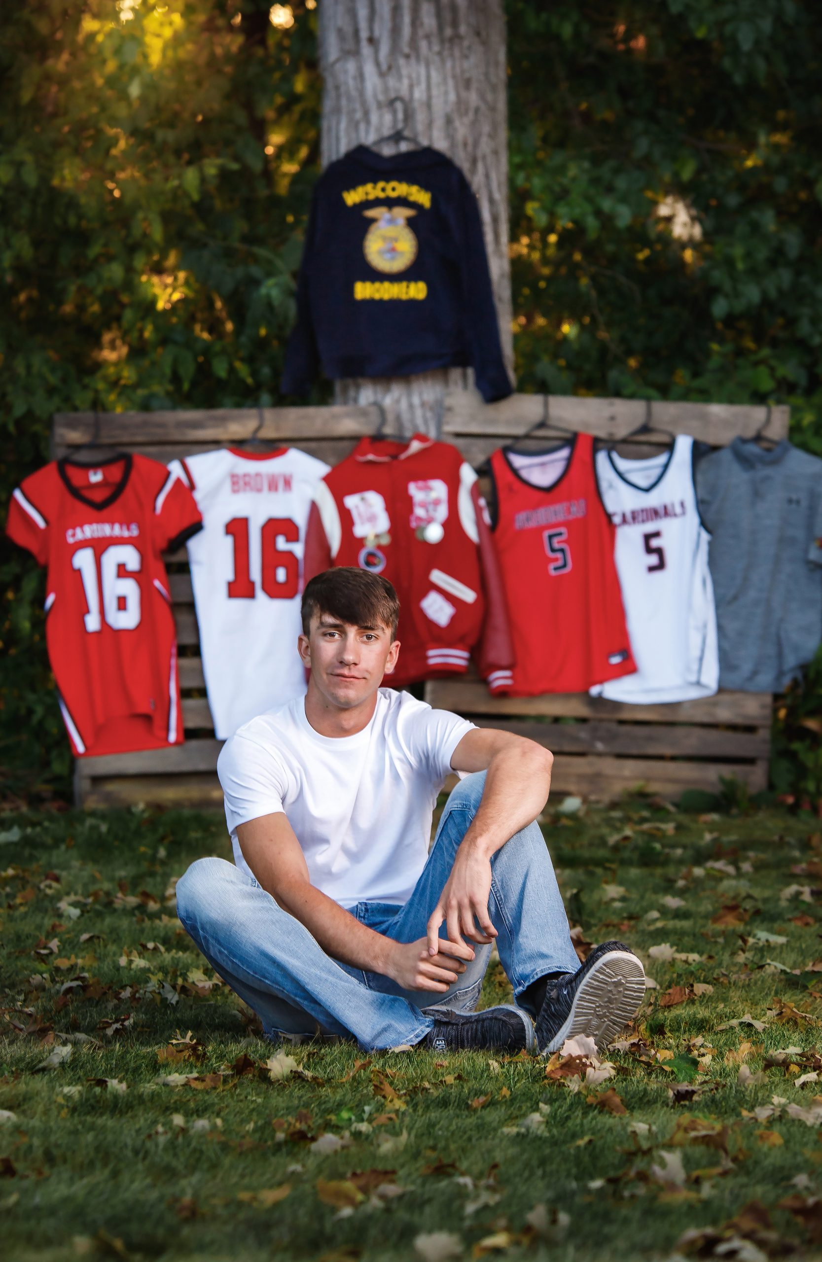 Photo of Brodhead, WI young man sitting for his senior pictures in front of wood pallets that have his sports jerseys and FFA jacket.  