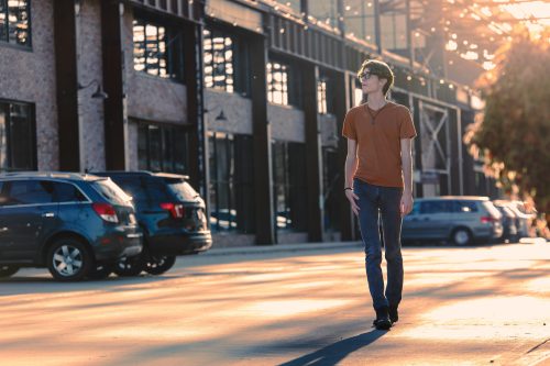 High school senior boy walking in a parking lot with sun behind him at the Ironworks Campus in Beloit, WI