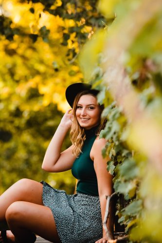High school senior girl portrait by Teri Lynn Photography at Olbrich Botanical Gardens. Young woman in a green dress and hat posing outdoors with a vibrant yellow and green natural background. Senior photography capturing natural beauty and personality